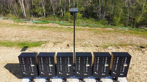 solar mailbox cluster light installed in front of a line of mailboxes in a wooded area.
